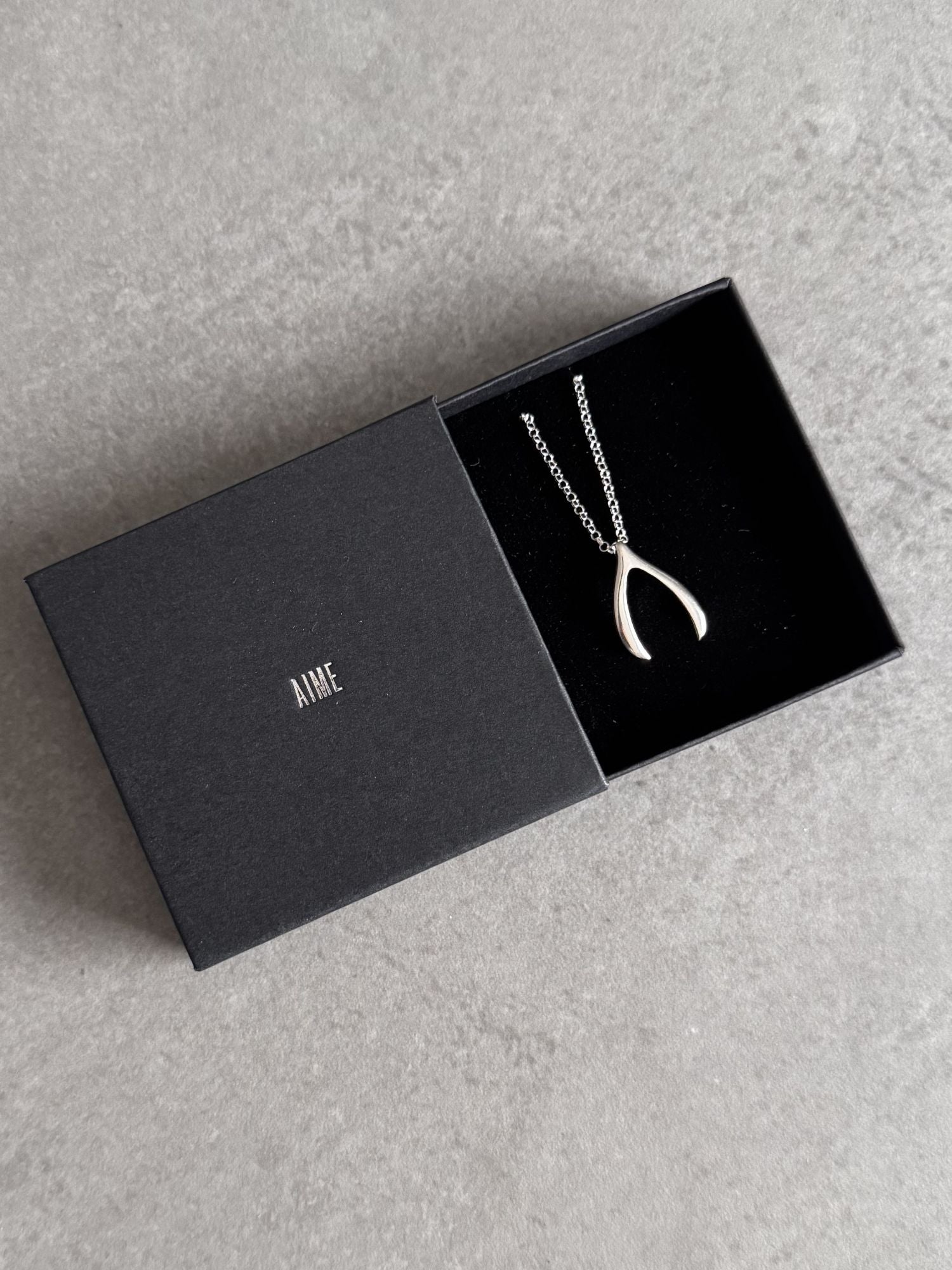 Sterling silver wishbone necklace presented in an open black Wue gift box.