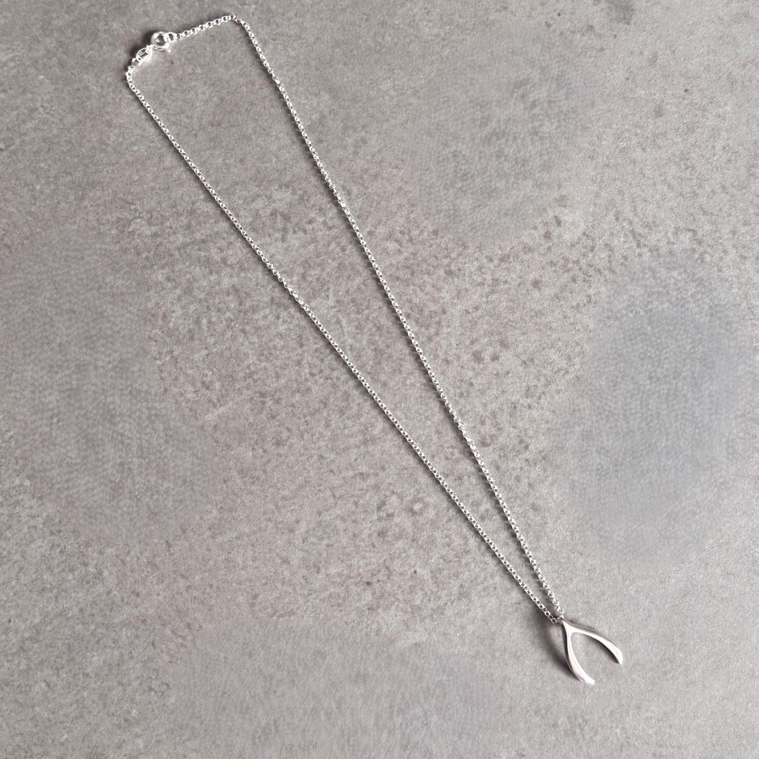 Sterling silver wishbone necklace laid out on a grey stone surface, showing the full chain and pendant.