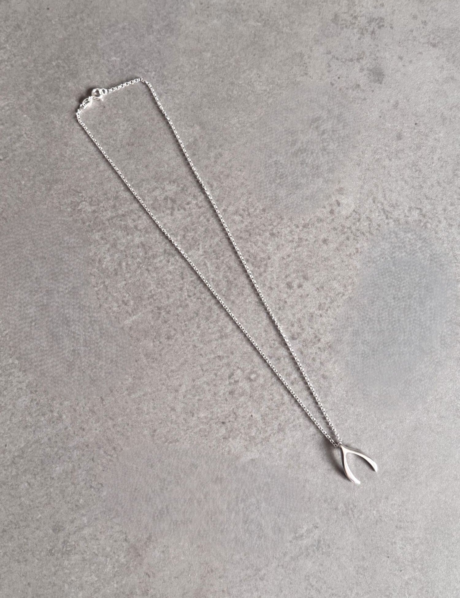 Sterling silver wishbone necklace laid out on a grey stone surface, showing the full chain and pendant.