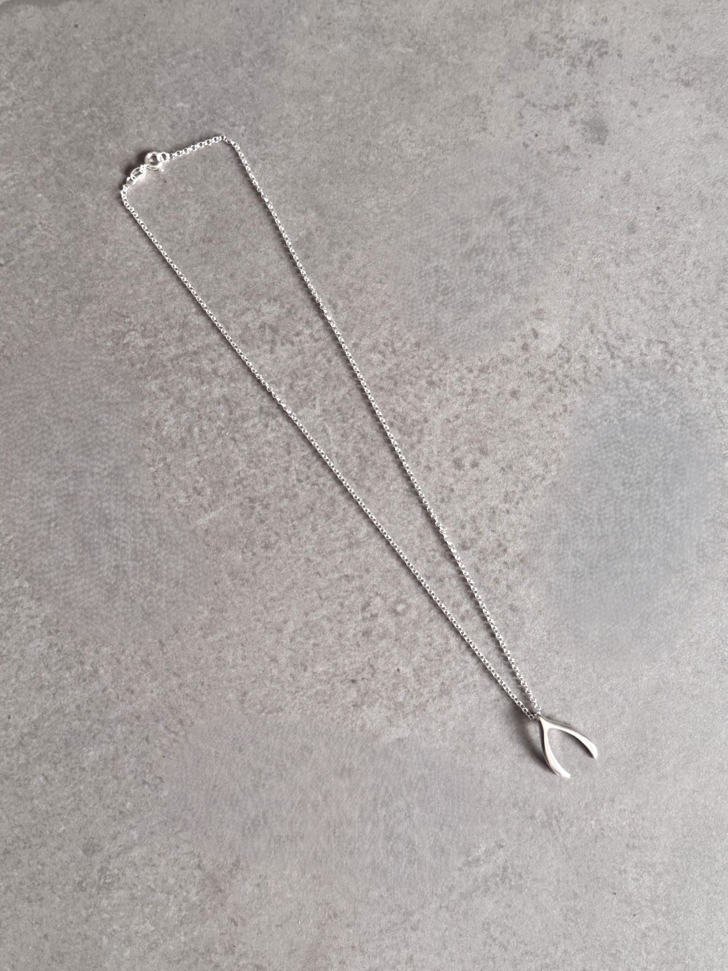 Sterling silver wishbone necklace laid out on a grey stone surface, showing the full chain and pendant.