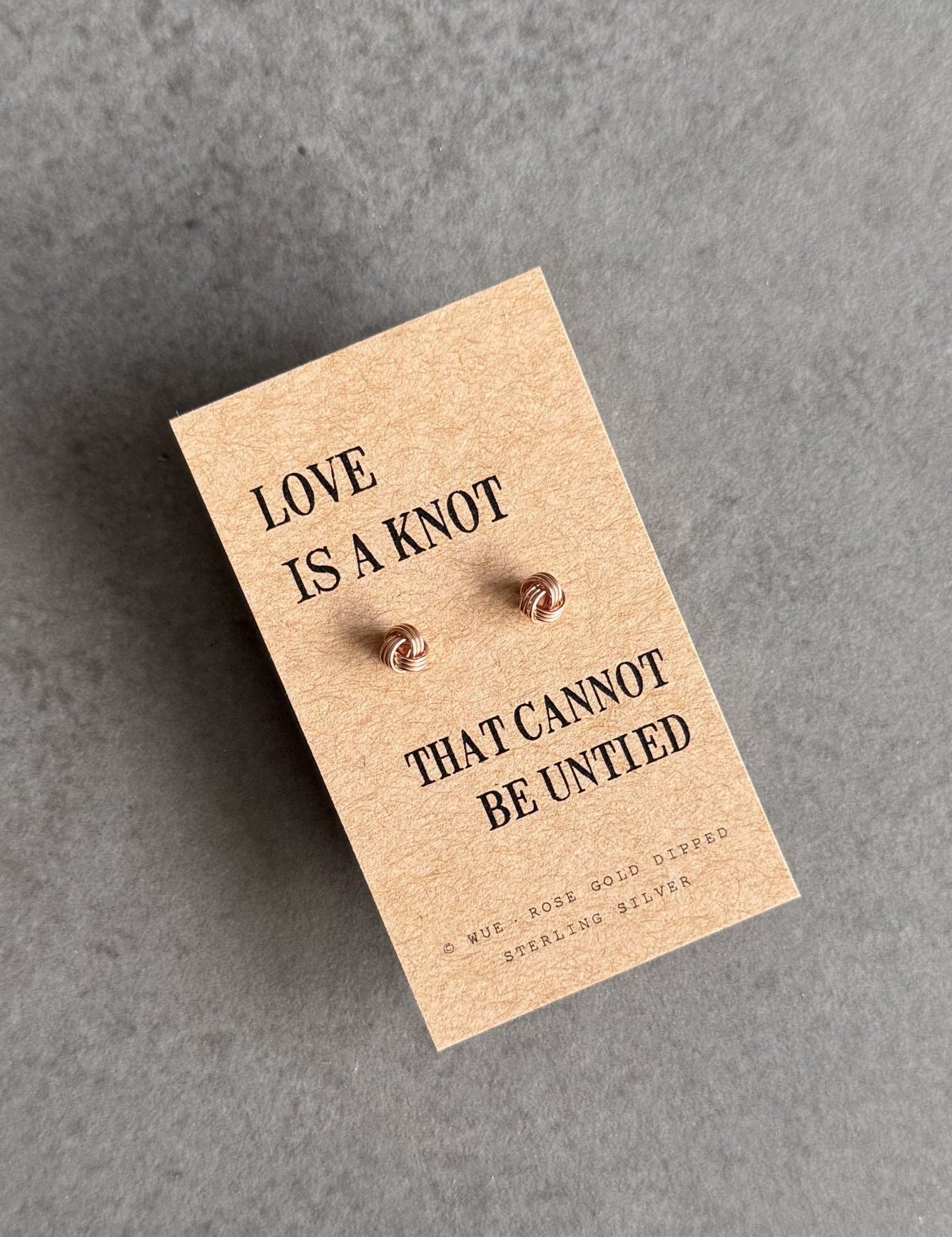 Pair of earrings on a card with 'Love is a knot that cannot be untied' text on a gray background