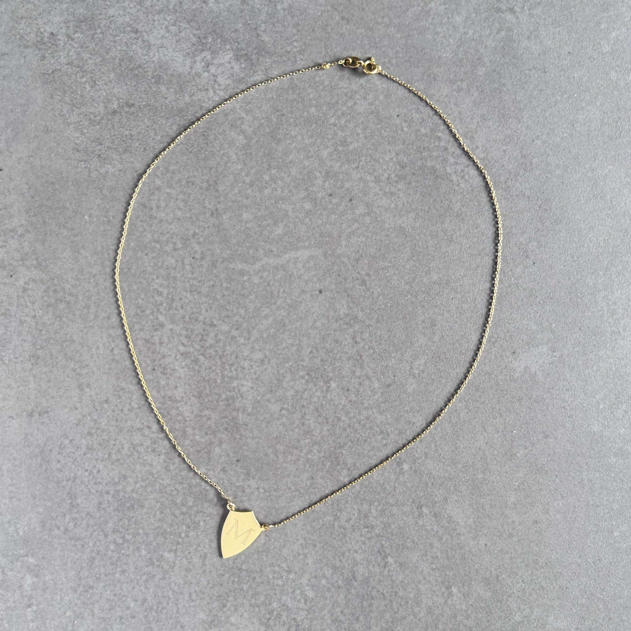 Gold plated shield necklace engraved with a single initial by By Wue