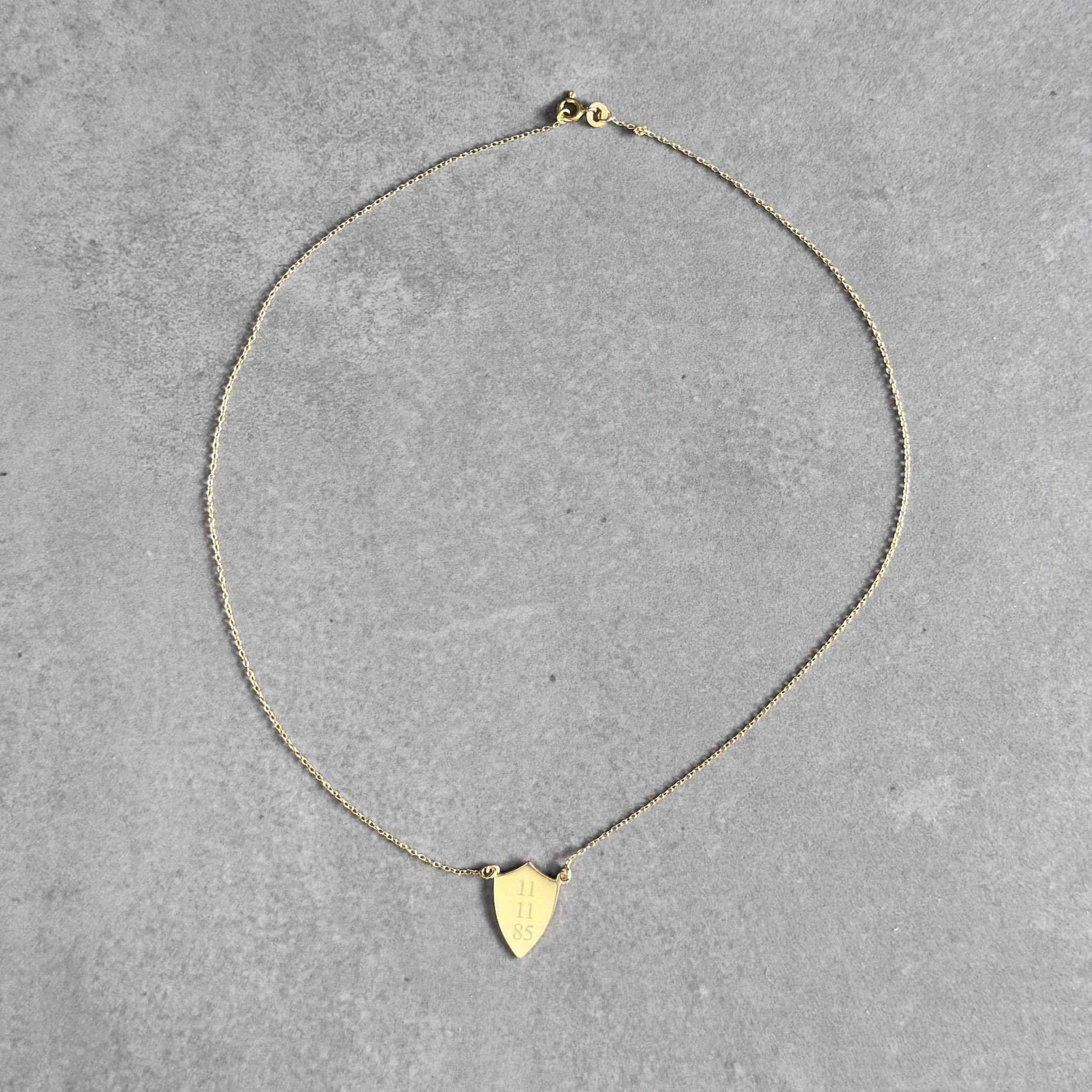 Gold plated shield necklace engraved with a date by By Wue