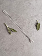Sterling silver wishbone pendant necklace on a grey stone surface, styled with sage leaves.
